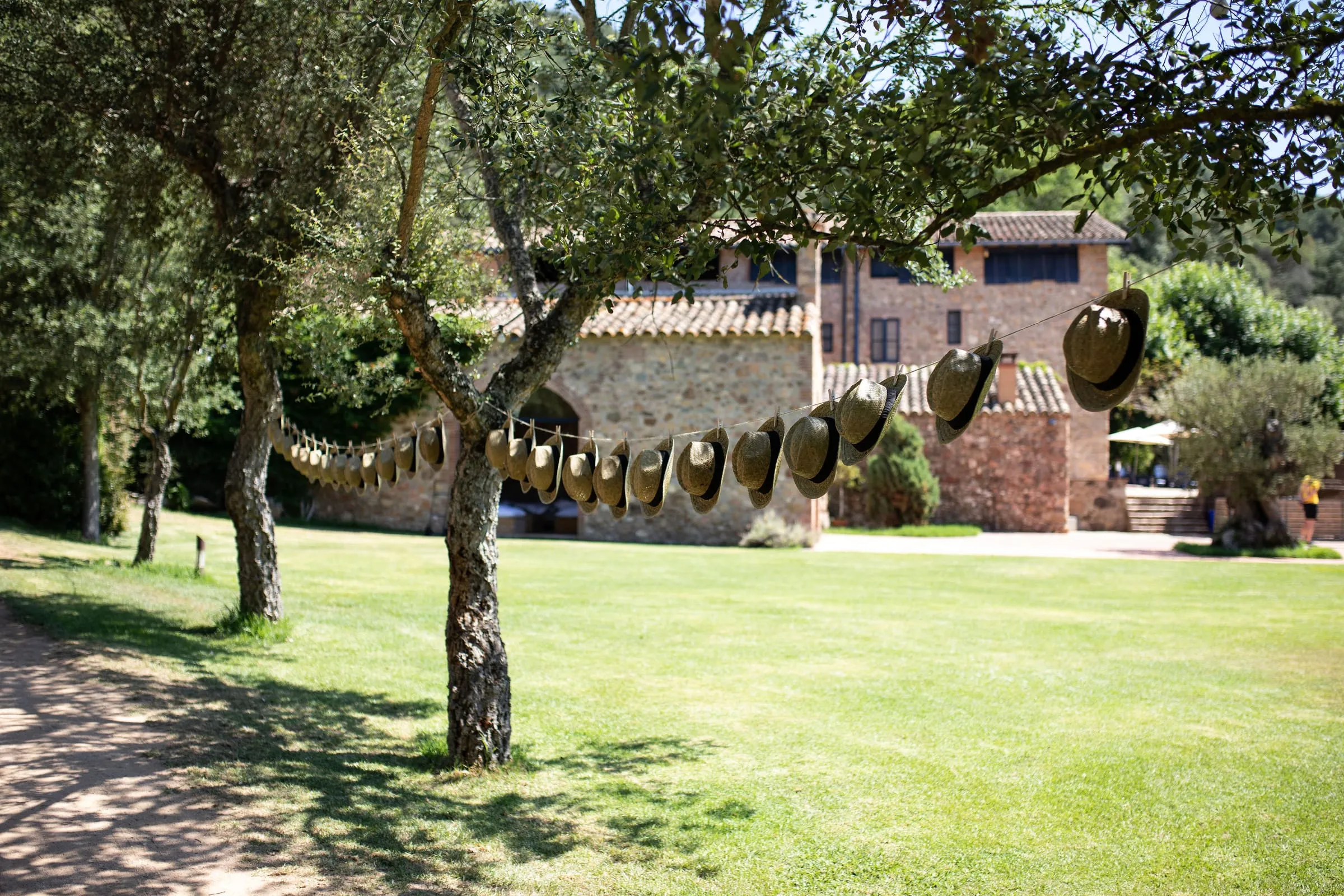Lawn garden with trees and low tables beside the stone farmhouse of Can Riera