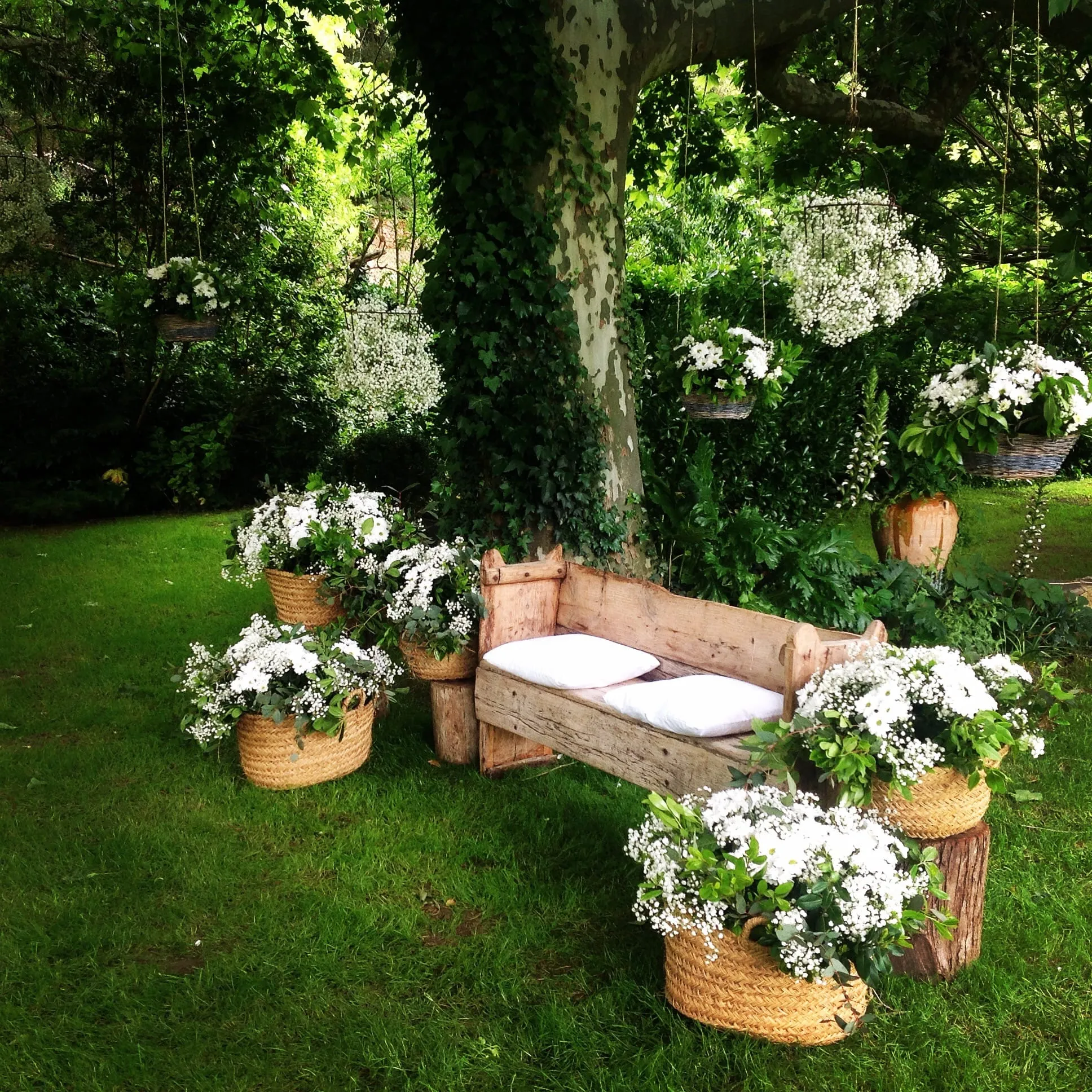 Banc de fusta amb cistells de flors blanques sota els arbres, preparat per a la cerimònia