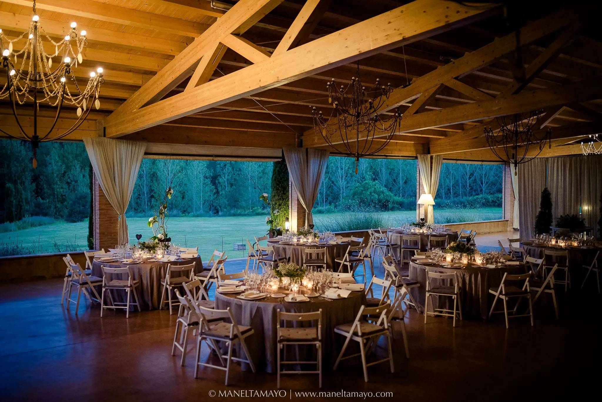 Saló de banquets amb bigues de fusta, taules rodones i cortines obertes al jardí