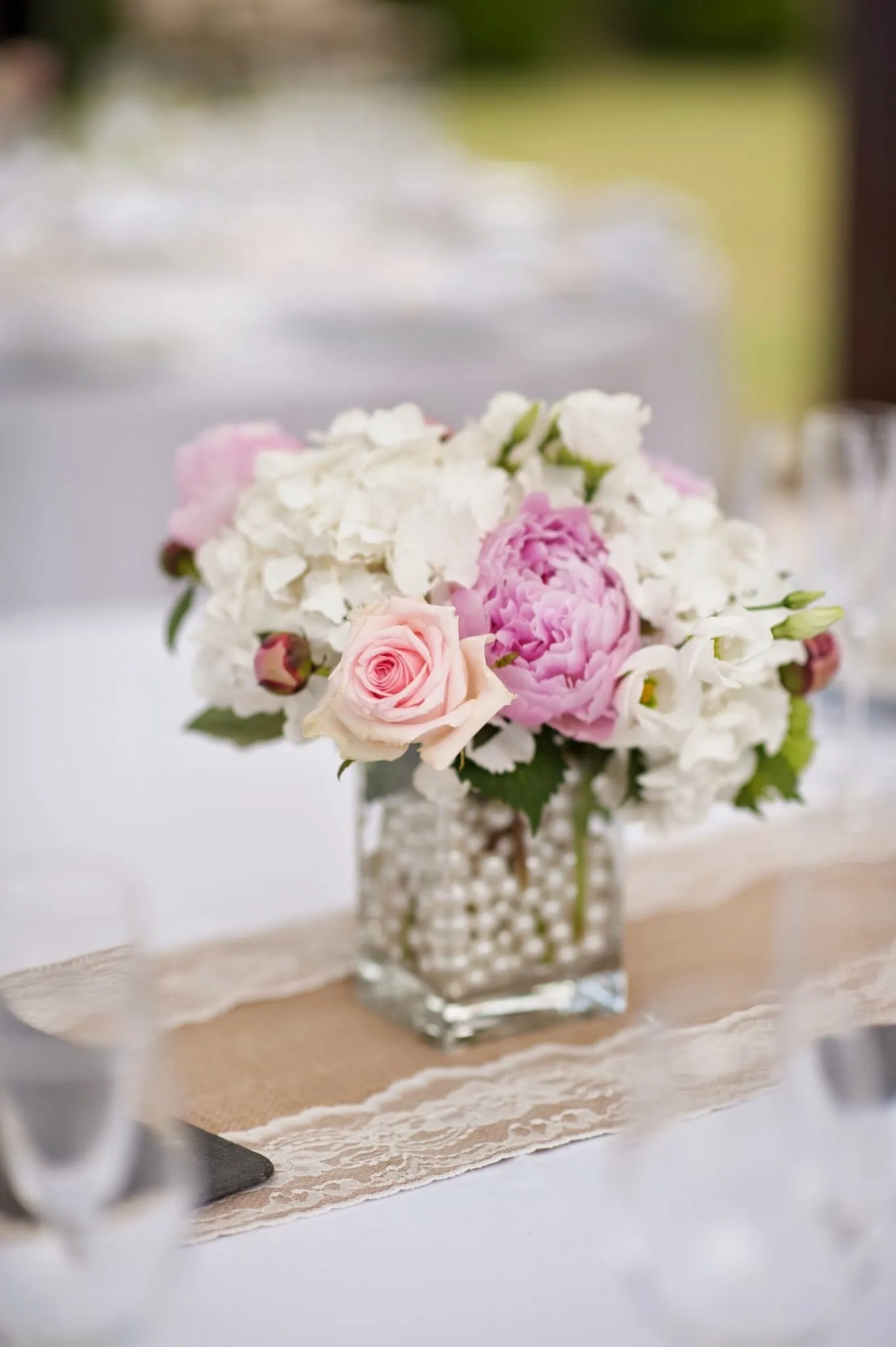 Small posy of pink roses and peonies in a glass vase filled with pearls