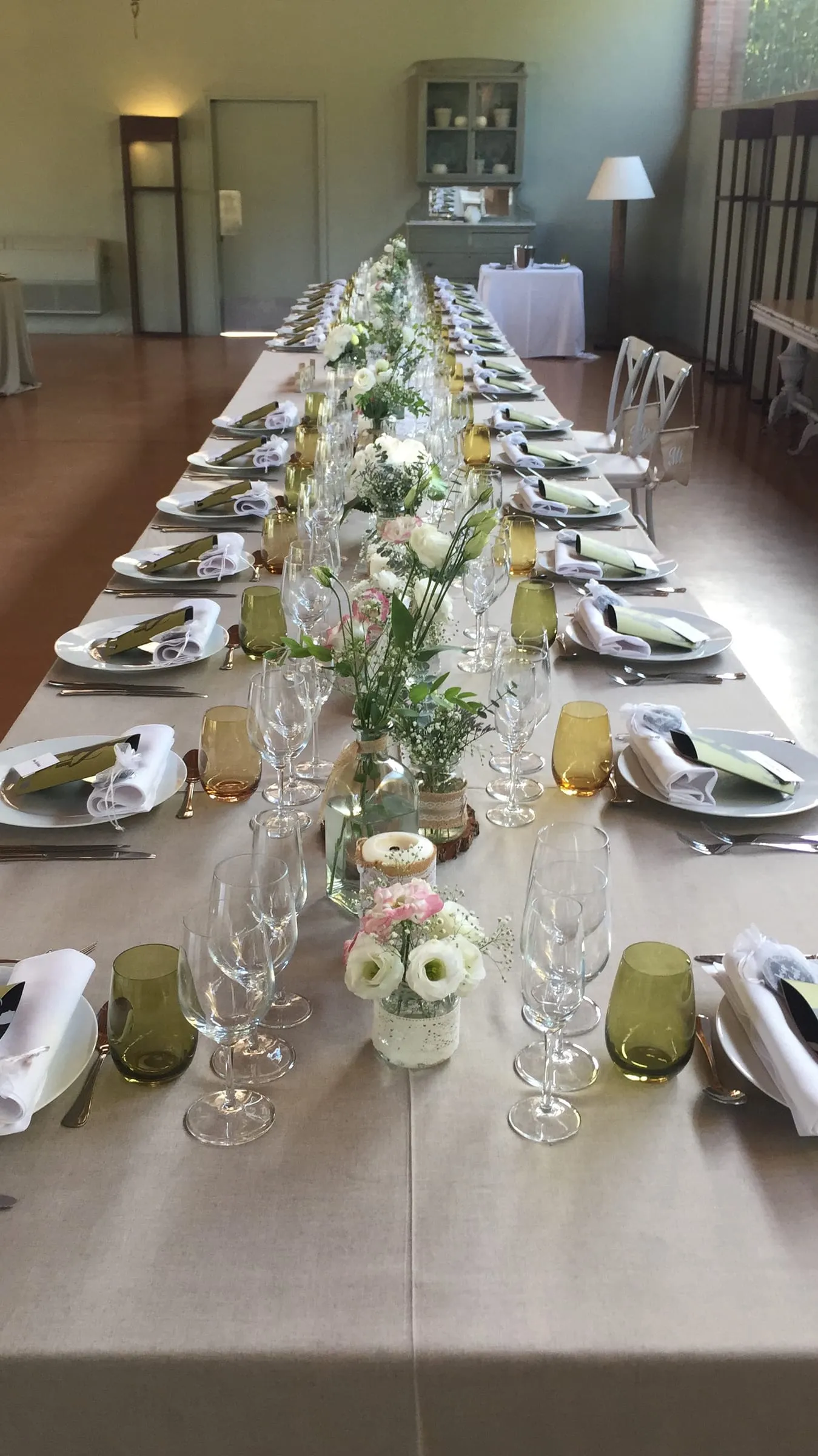 Taula de banquet llarga amb estovalles blanques, copes de vidre verd i petits rams de flors blanques