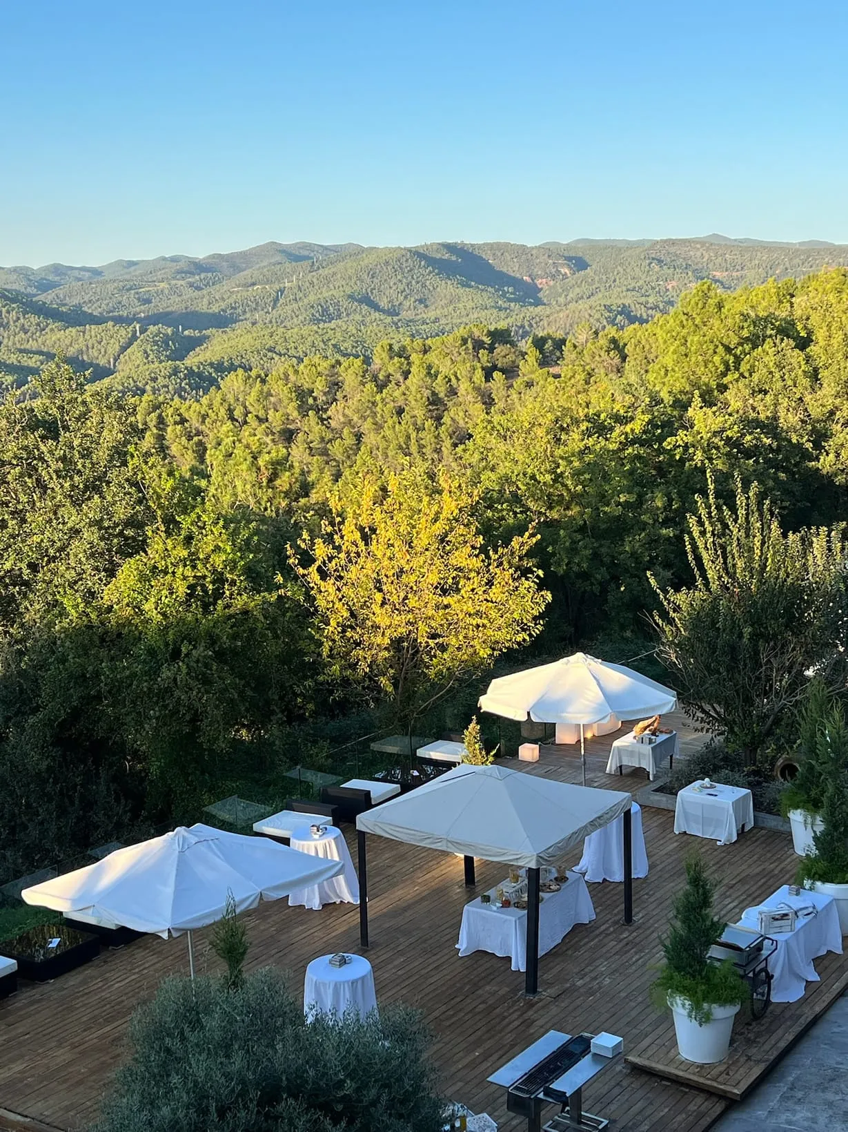 Wooden terraces with white parasols among the trees, with the valley and mountains behind