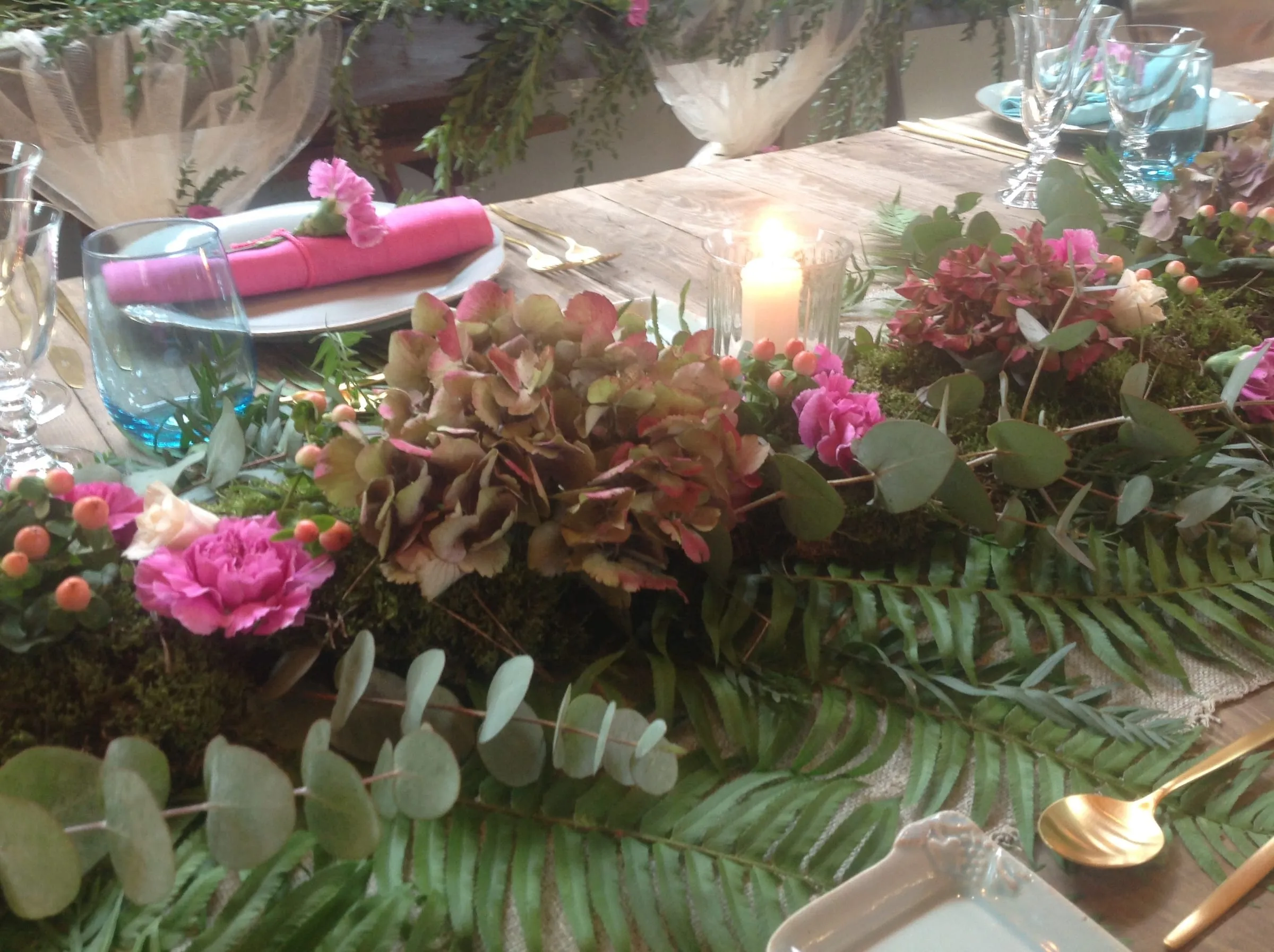 Table with an arrangement of hydrangeas and roses, a lit candle and a pink napkin