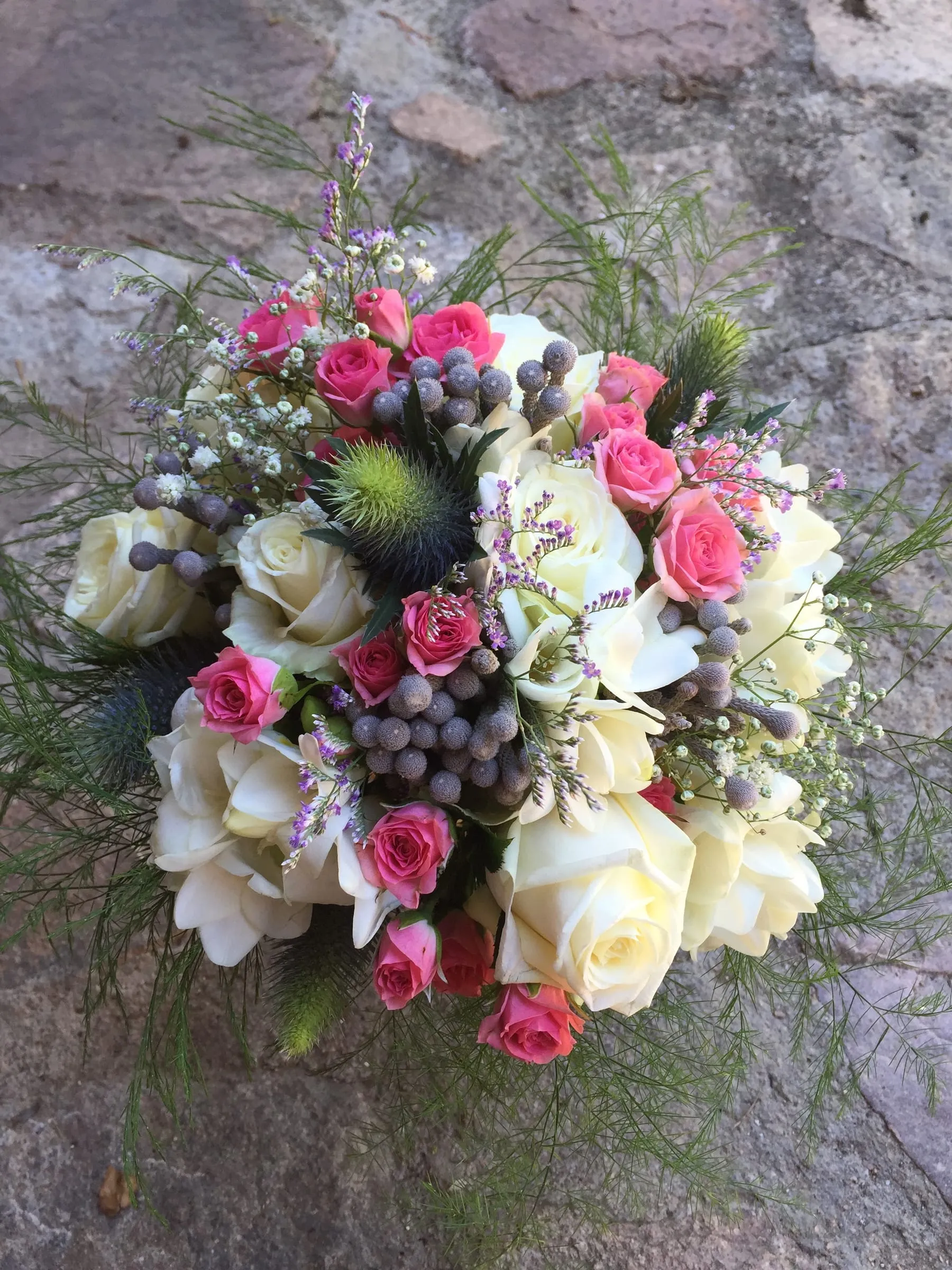 Bridal bouquet of white and pink roses with blue thistles and green leaves